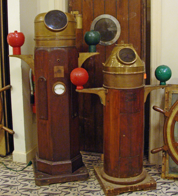 Antique ship binnacles stand guard in front of an antique ships door.